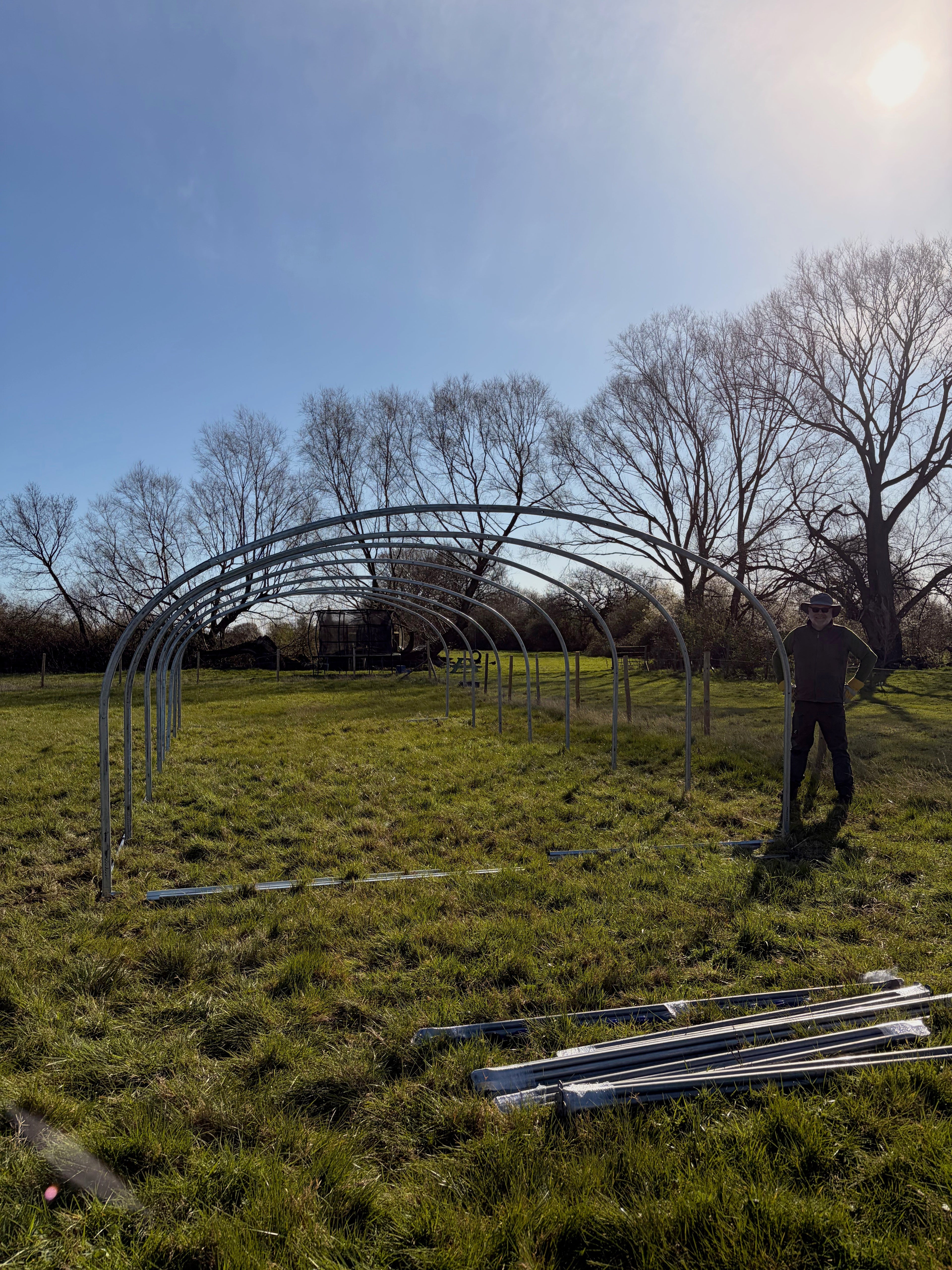 A partially built polytunnel frame with Martin from Yorkshire Edible Flowers stood next to it