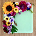 Colourful edible flowers on a square cake iced with light green fondant on a  wooden surface.