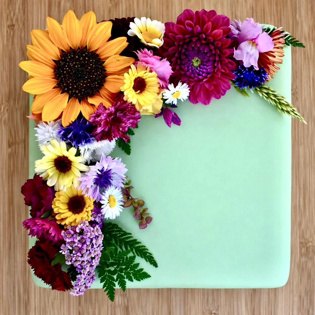 Colourful edible flowers on a square cake iced with light green fondant on a  wooden surface.