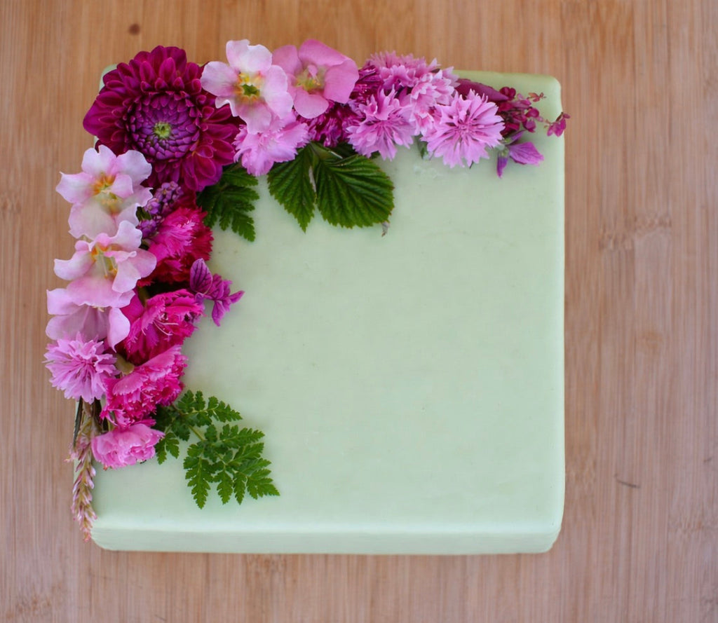 Pink edible flowers on a square cake iced with light green fondant icing on a wooden board