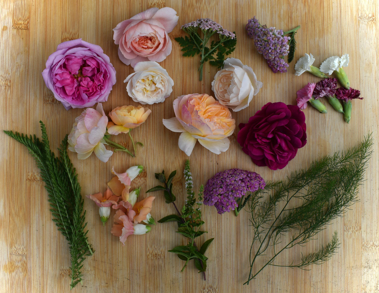 Assorted edible roses and foliage on a wooden surface
